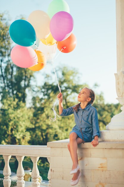 Mädchen, das bunte Luftballons hält, die zu ihnen schauen