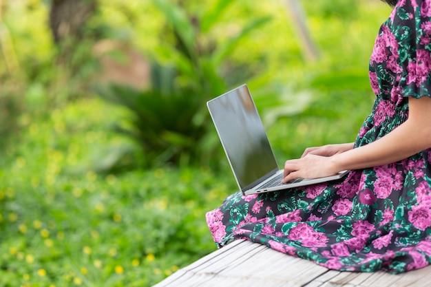 Mädchen, das ein Blumenkleid sitzt mit ihrem Laptop trägt