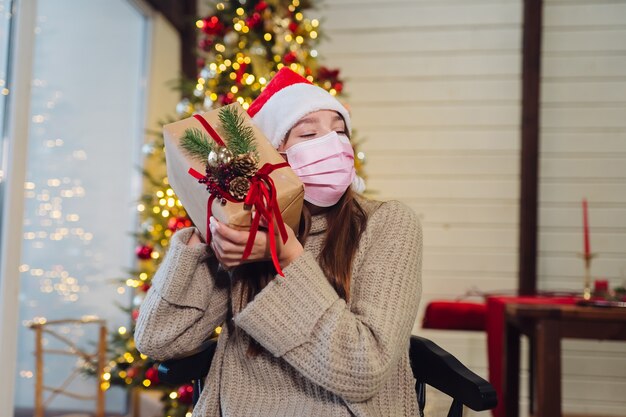 Mädchen, das ein Weihnachtsgeschenk am Silvesterabend hält. Mädchen, das in die Kamera schaut. Weihnachten während Coronavirus, Konzept