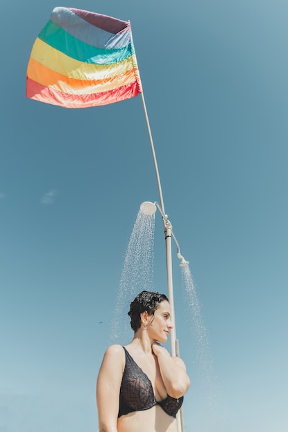 Mädchen, das eine Dusche im Strand unter einer spinnenden lgbt Flagge hat