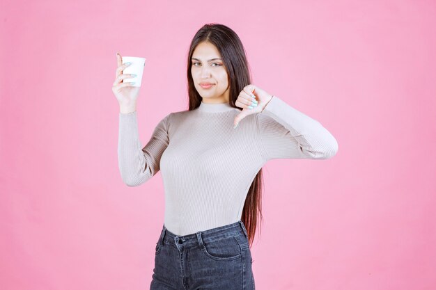 Mädchen, das eine Kaffeetasse hält und Daumen nach unten zeigt