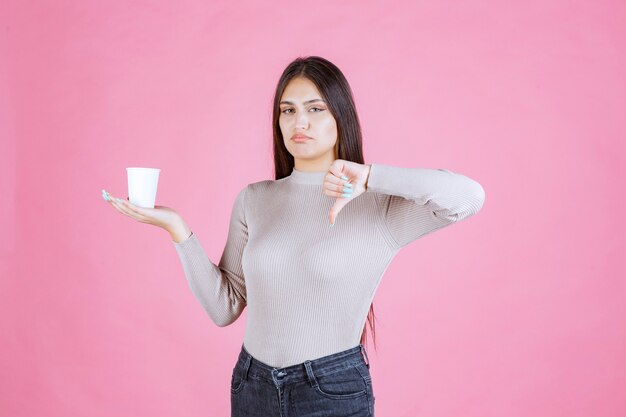 Mädchen, das eine Kaffeetasse hält und Daumen nach unten zeigt