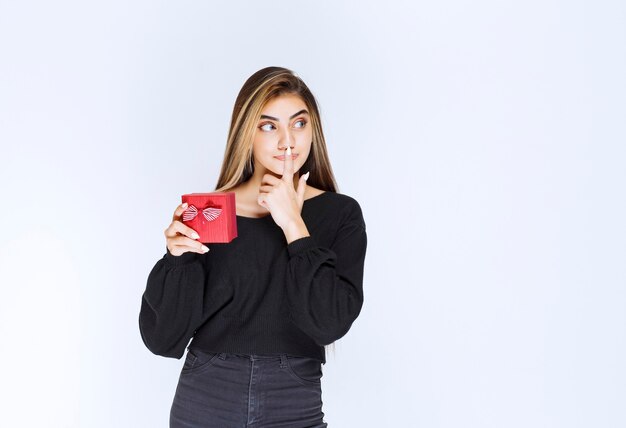 Mädchen, das eine rote Geschenkbox hält und denkt oder zögert. Foto in hoher Qualität