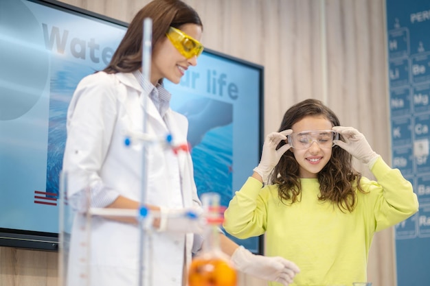 Mädchen, das eine Schutzbrille anprobiert, die in der Nähe des Lehrers steht