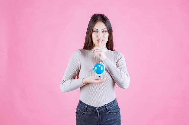 Mädchen, das einen Globus hält und Schweigenzeichen macht