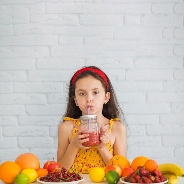 Mädchen, das Erdbeeresmoothies mit reifen Früchten über dem Schreibtisch trinkt