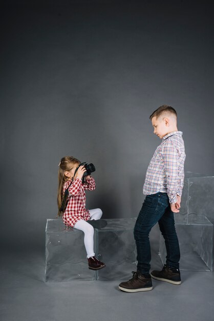 Mädchen, das Foto eines Jungen mit Kamera gegen grauen Hintergrund macht