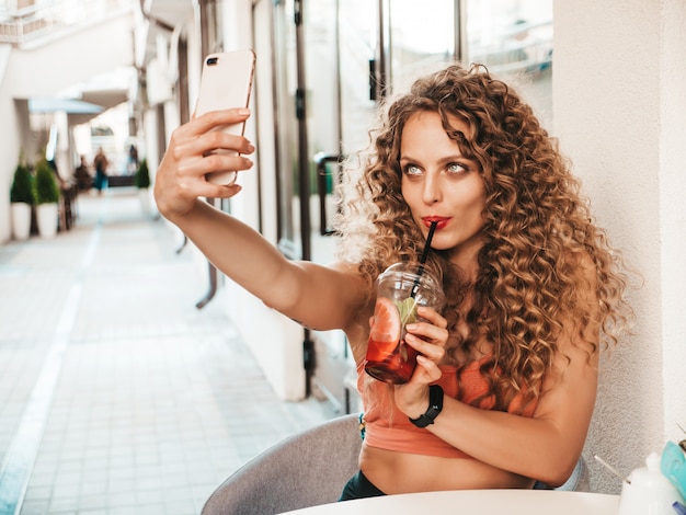 Mädchen, das frischen Smoothie im Plastikbecher mit Strohhalm trinkt und ein selfie nimmt