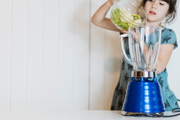 Kostenloses Foto mädchen, das früchte zur mischmaschine setzt