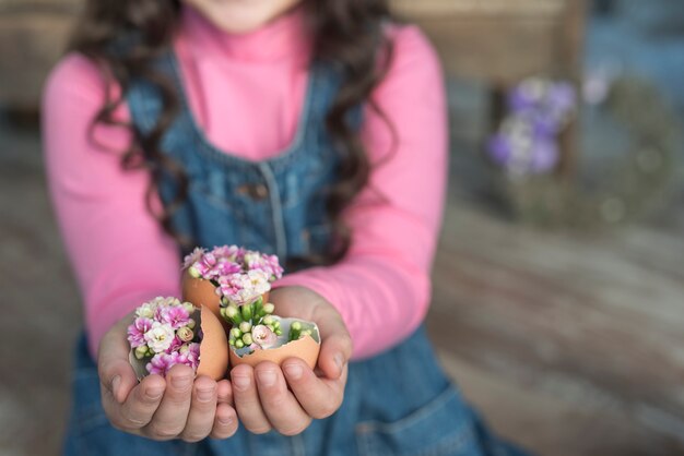 Mädchen, das gebrochene Eier mit Blumen in den Händen hält