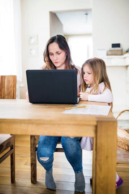 Mädchen, das ihre Mutter verwendet Laptop auf Holztisch betrachtet