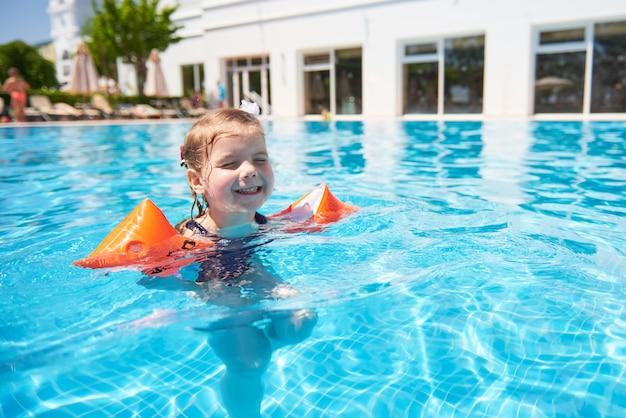 Mädchen, das im Pool in Armbinden an einem heißen Sommertag schwimmt. Familienurlaub in einem tropischen Resort