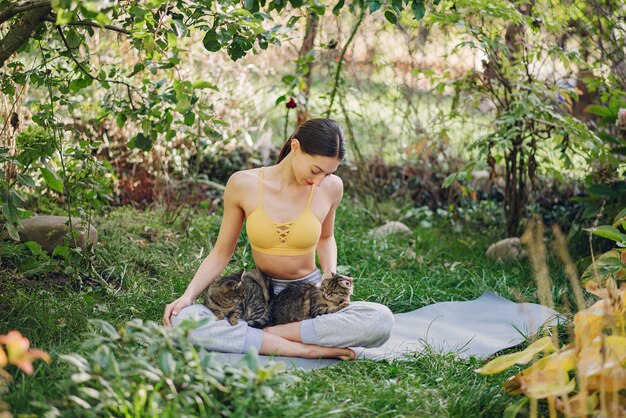 Mädchen, das in einem Sommerpark mit niedlicher Katze sitzt