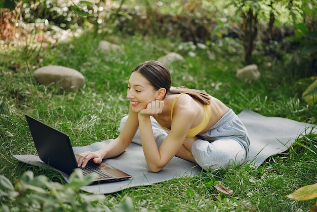 Mädchen, das in einem Sommerpark sitzt und einen Laptop in ihren Händen hält