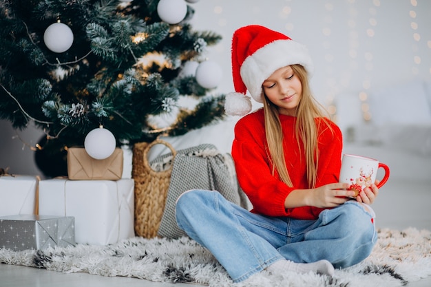 Mädchen, das Kakao durch Weihnachtsbaum trinkt