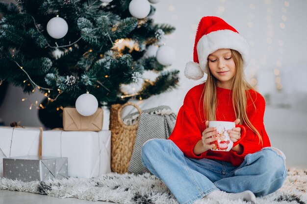 Mädchen, das Kakao durch Weihnachtsbaum trinkt