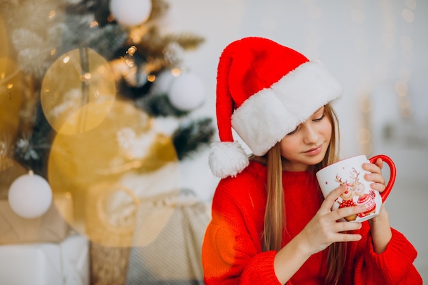 Mädchen, das kakao durch weihnachtsbaum trinkt