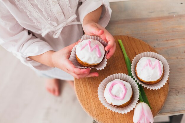 Mädchen, das kleinen Kuchen mit Mutteraufschrift hält