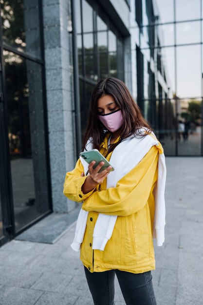 Mädchen, das Maske trägt, die auf Straße aufwirft. Mode beim Ausbruch des Coronavirus.