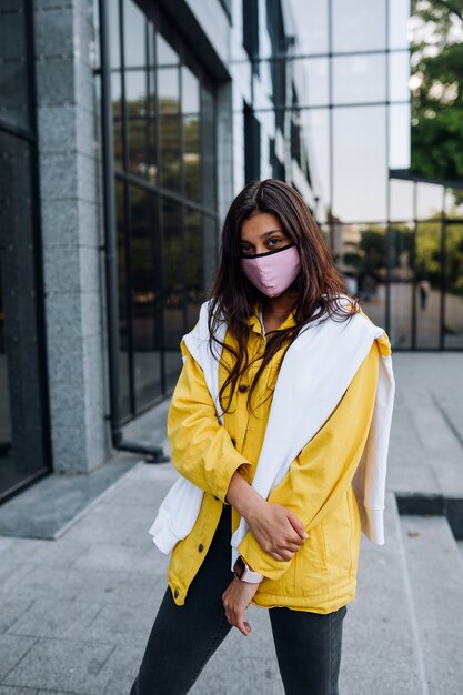 Mädchen, das Maske trägt, die auf Straße aufwirft. Mode während der Quarantäne des Coronavirus-Ausbruchs.