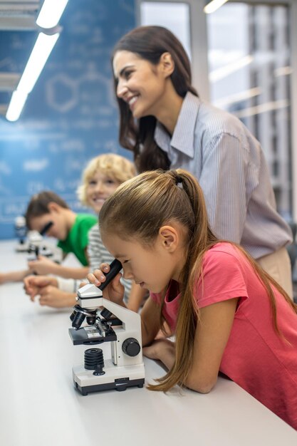 Mädchen, das mit Jungen durch Mikroskop und Lehrer schaut