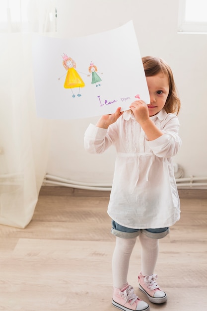 Kostenloses Foto mädchen, das mit zeichnung der mutter und des kindes steht