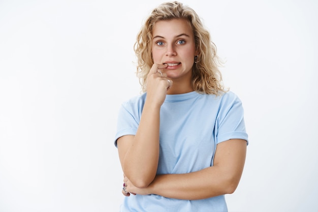 Mädchen, das nachgedacht hat, sich eine Lösung auszudenken, den Finger auf die Lippen zu halten und die Zähne zu zeigen, um die Wahl zu treffen, zu entscheiden, wie es sich konzentriert und nervös über der weißen Wand posiert, Mut sammelt, um zu sagen