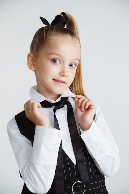 Mädchen, das sich nach einer langen Sommerpause auf die Schule vorbereitet. Zurück zur Schule. Kleines weibliches kaukasisches Modell, das in der Schuluniform auf weißem Studiohintergrund aufwirft. Kindheit, Bildung, Ferienkonzept.