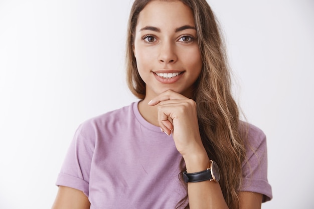 Mädchen, das sorgfältig interessante Geschichte hört. Fröhliche, begeisterte, neugierige, gut aussehende Studentin, die eine tolle faszinierende Geschichte hört, die beteiligt aussieht, erfreut lächelt und nachdenklich das Kinn berührt