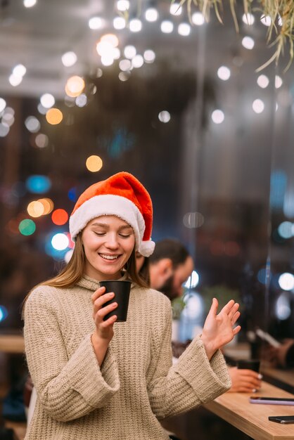 Mädchen, das Weihnachtsmannhut trägt, der im Kaffeehaus sitzt und Kaffee trinkt