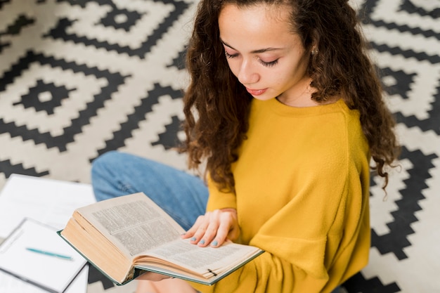 Kostenloses Foto mädchen des hohen winkels, das zuhause ein buch liest