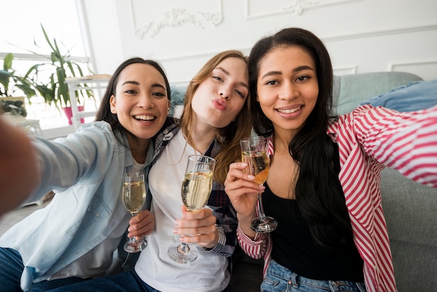 Mädchen, die Gläser mit Getränk halten und selfies nehmen