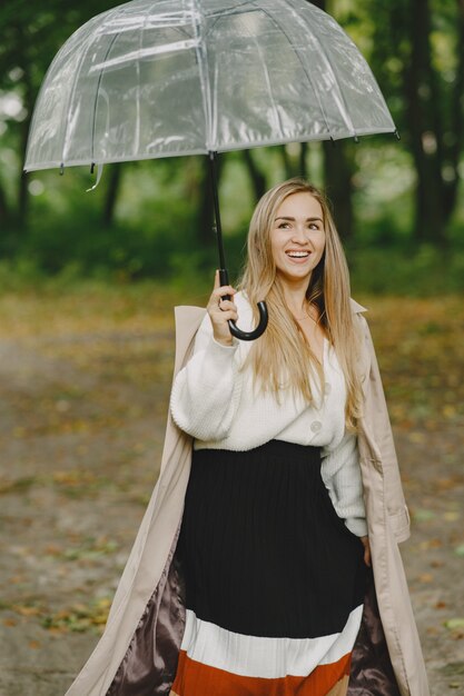 Mädchen geht. Frau in einem braunen Mantel. Blond mit Regenschirm.