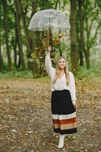 Mädchen geht. Frau in einem weißen Pullover. Blond mit Regenschirm. Fallende Blätter.