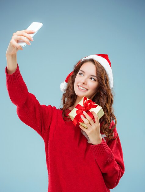 Mädchen gekleidet in Weihnachtsmütze mit einem Weihnachtsgeschenk und Telefon.