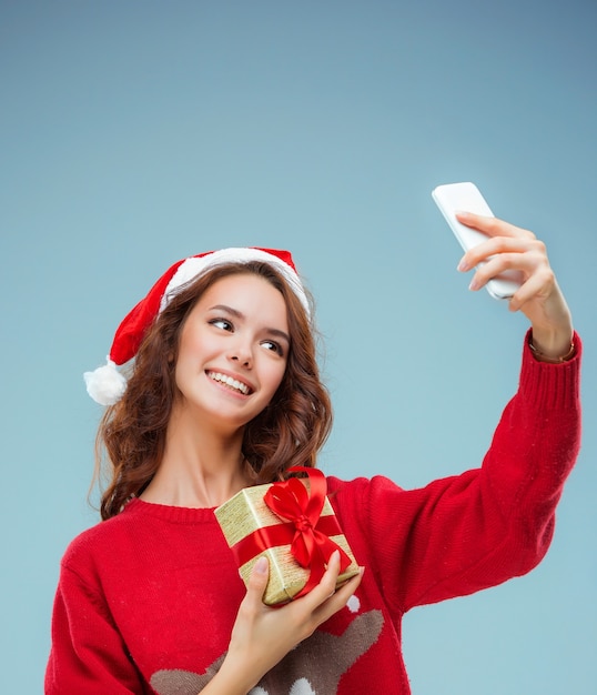 Mädchen gekleidet in Weihnachtsmütze mit einem Weihnachtsgeschenk und Telefon