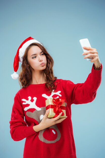 Mädchen gekleidet in Weihnachtsmütze mit einem Weihnachtsgeschenk und Telefon