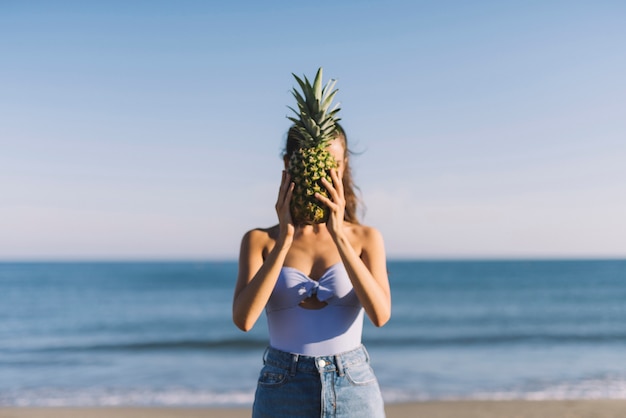 Mädchen hält Ananas vor Gesicht