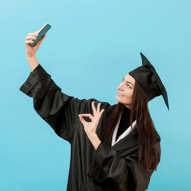 Mädchen im akademischen Anzug, das selfie nimmt