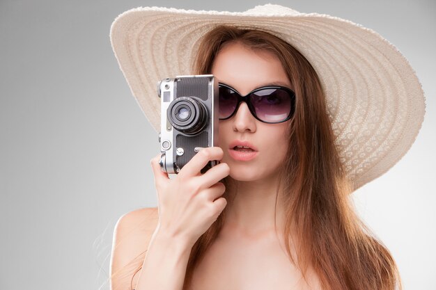 Mädchen im breitkrempigen Hut und in der Sonnenbrille mit Retro- Kamera