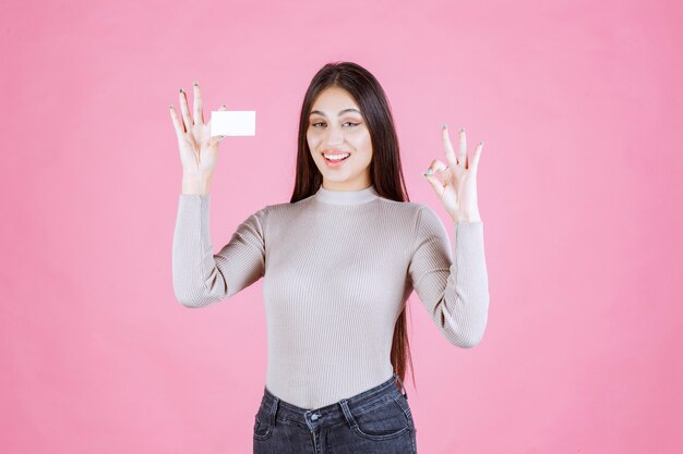 Mädchen im grauen Pullover zeigt ihre neue Visitenkarte, die gutes Handzeichen macht