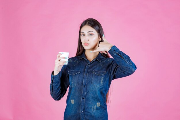 Mädchen im Jeanshemd, das eine Kaffeetasse hält und Rufzeichen macht