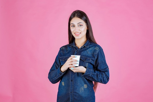 Mädchen im Jeanshemd, das eine wegwerfbare Tasse Kaffee genießt