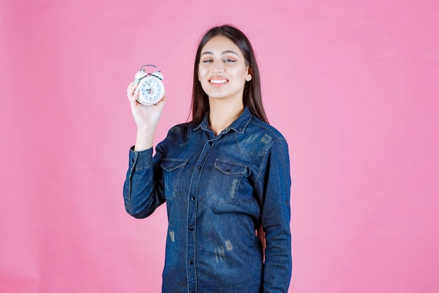 Mädchen im jeanshemd, das einen wecker hält und fördert