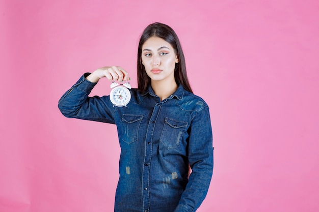 Mädchen im jeanshemd, das einen wecker hält und fördert