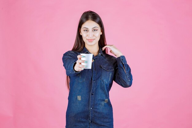 Mädchen im Jeanshemd, das ihrem Freund eine Tasse Kaffee anbietet