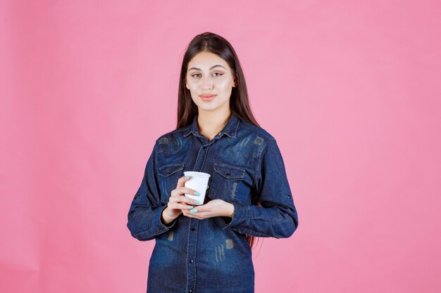Mädchen im Jeanshemd hält eine Kaffeetasse und fühlt sich positiv