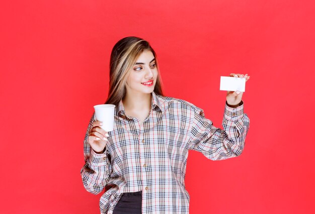 Mädchen im karierten Hemd hält eine Kaffeetasse und präsentiert ihre Visitenkarte