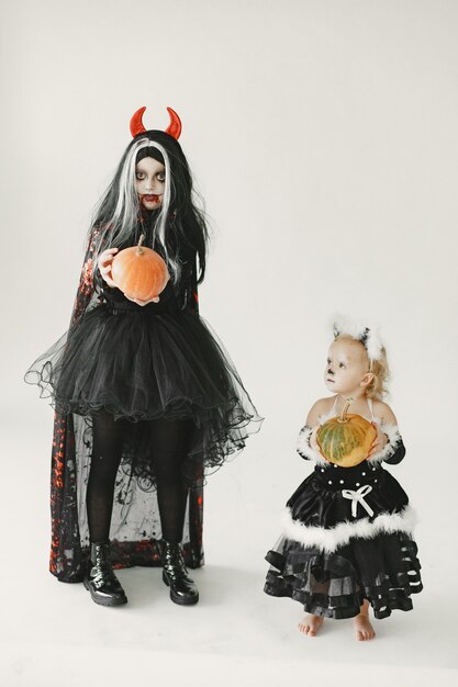Mädchen im Kostüm des Teufels, das neben einem kleinen Mädchen steht, das im schwarzen Kleid als Katze gekleidet ist