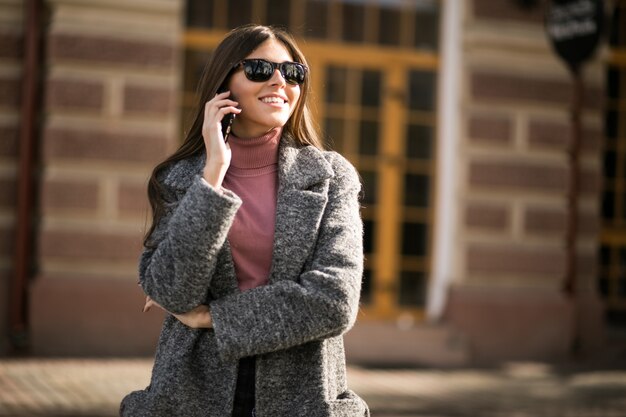 Mädchen im Mantel mit dem Telefon, das in der Straße steht